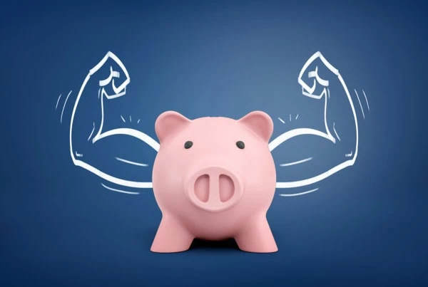 a piggy bank standing in front of a drawing that makes the piggy bank look like it has muscles.