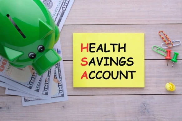 a green piggy bank sits to the left of a post-it note that says health savings account.