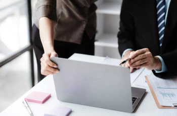 a pair of fund managers look at charts and a laptop computer.