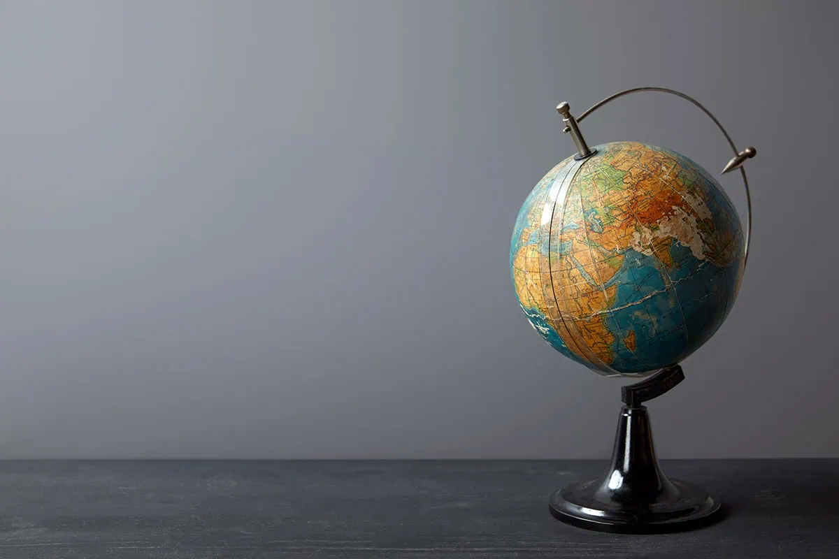 a school globe of the world sits on a wood floor against a gray background.