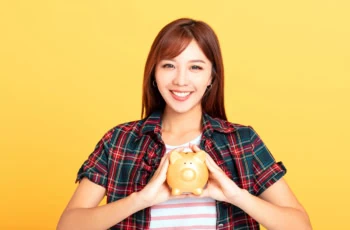 a younger asian woman holds a piggy bank in her hands.