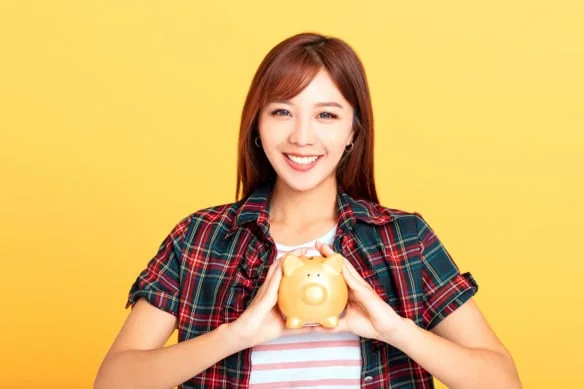 a younger asian woman holds a piggy bank in her hands.