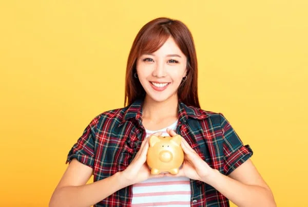 a younger asian woman holds a piggy bank in her hands.