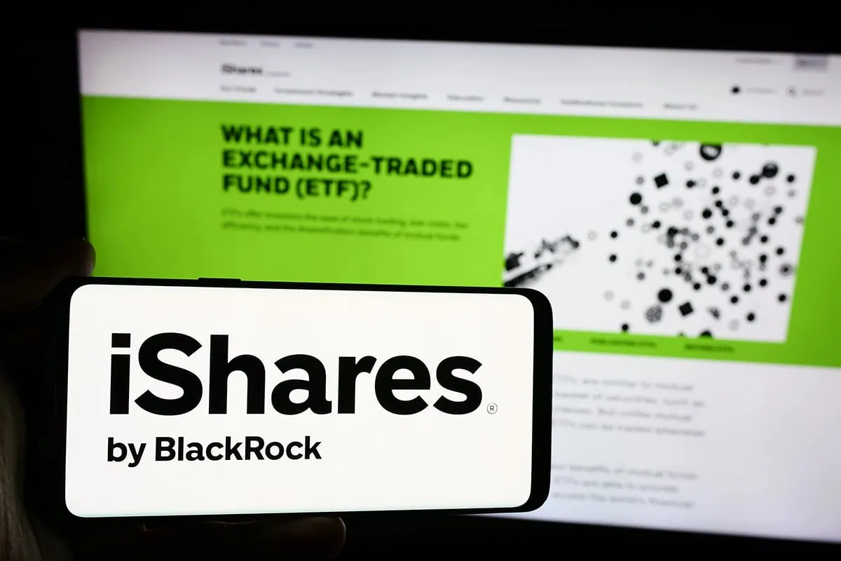 a phone showing the ishares logo is held in front of a computer showing the ishares website.