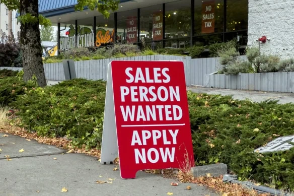 a help wanted sign sits outside of a store.
