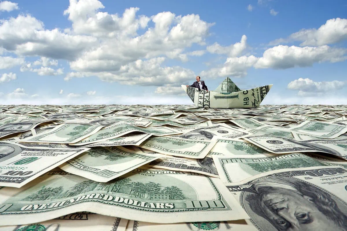 a businessman sails on a sea of cash in a boat made out of cash.