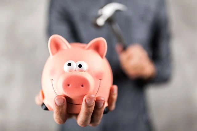 Man holding a piggy bank with hammer in background