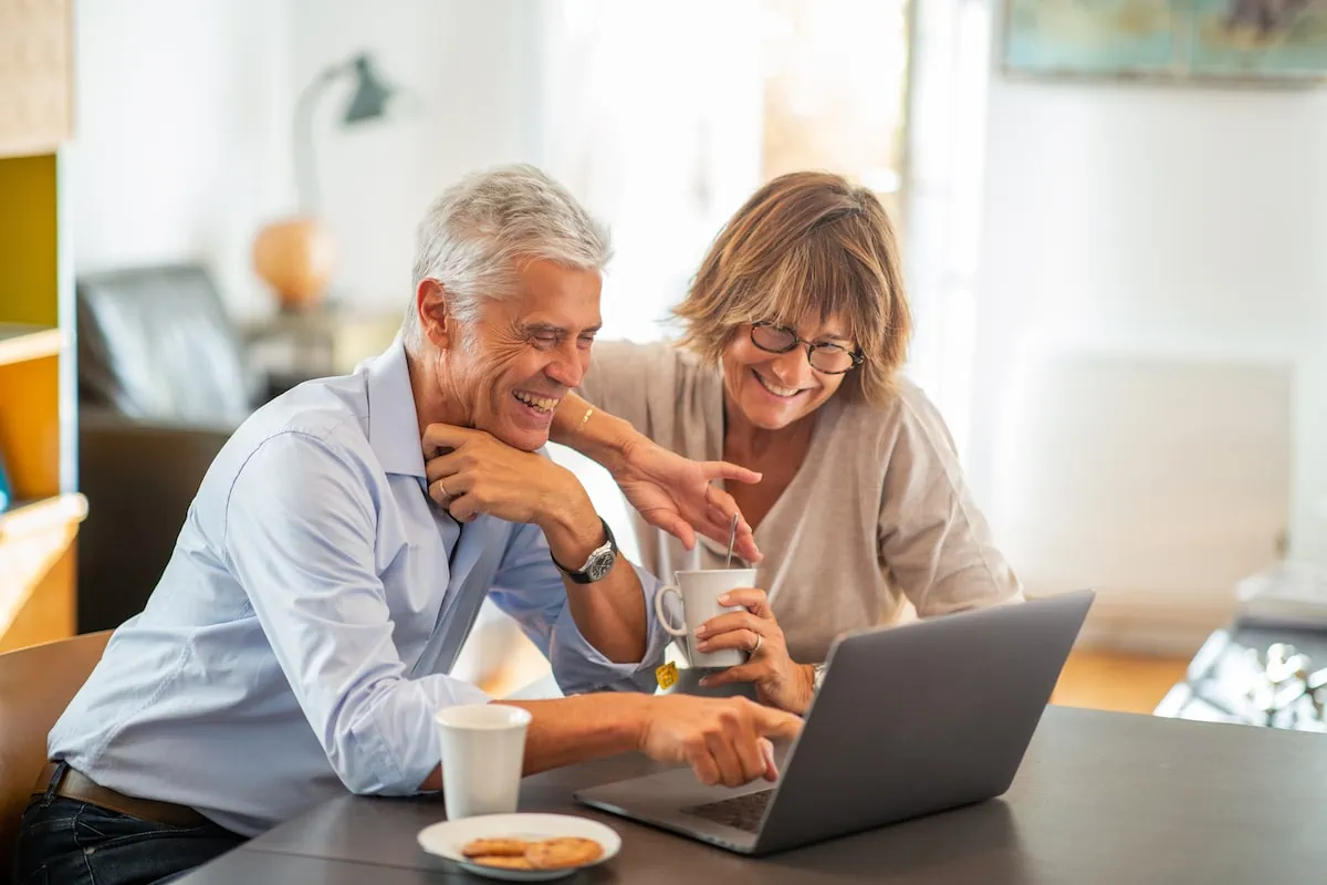 smiling older couple sitting at table looking at laptop