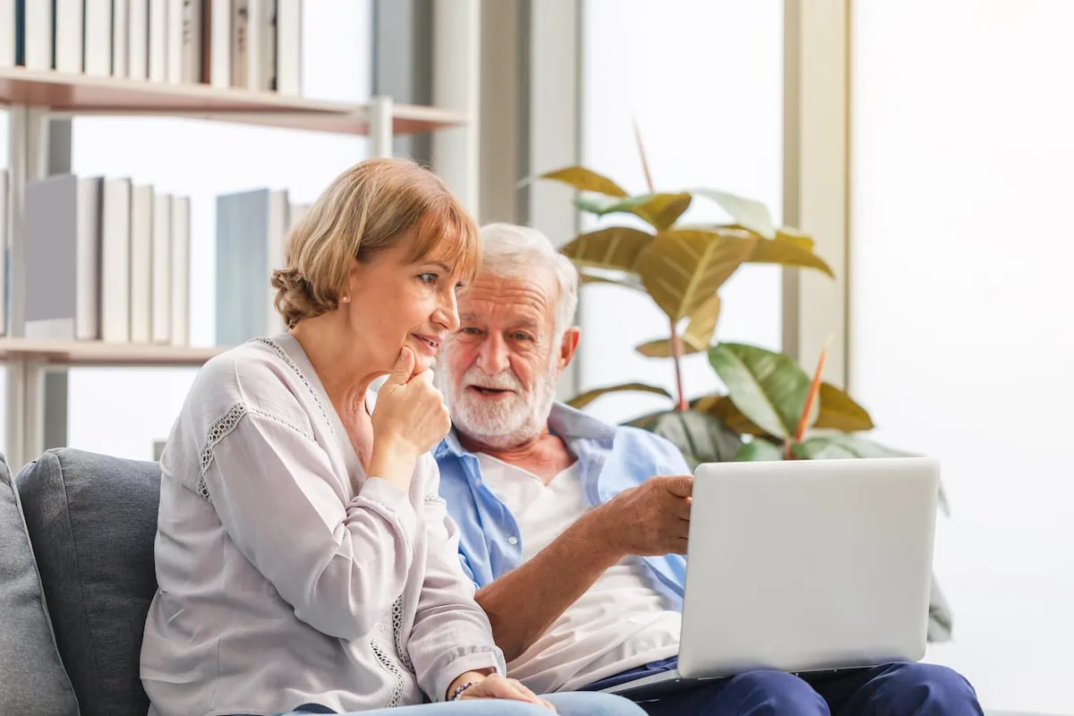 Portrait of happy senior couple in living room, Elderly woman and a man using computer laptop on cozy sofa at home, Happy family concepts