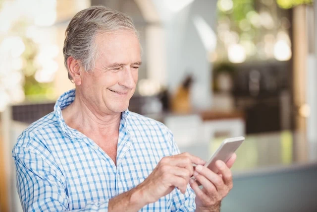 Happy senior man using mobile phone at home