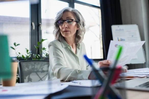 mature woman looking at spreadsheets at desk-1200