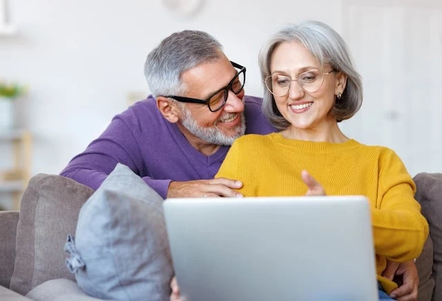 Beautiful mature family couple looking at laptop with smile on face while spending time together