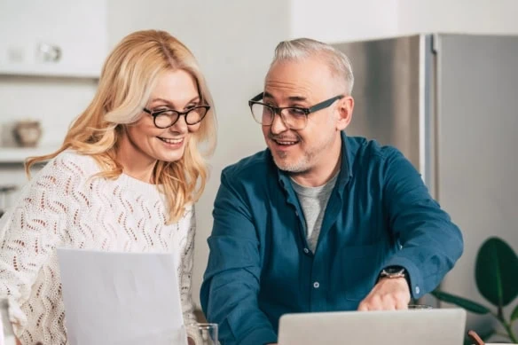 middle-aged couple reviewing documents together at laptop smiling