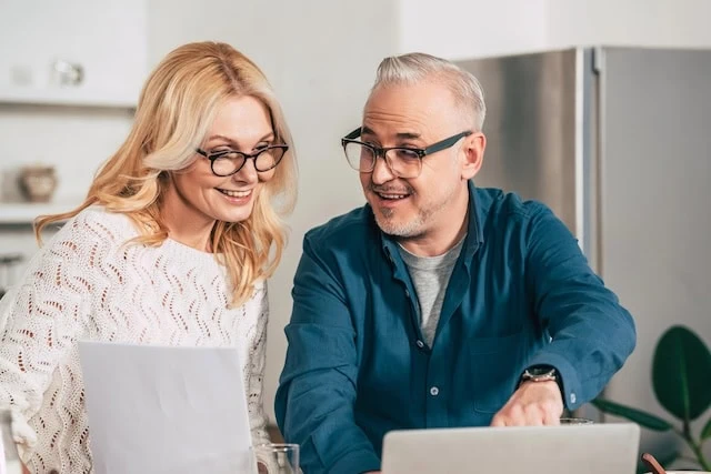 middle-aged couple reviewing documents together at laptop smiling