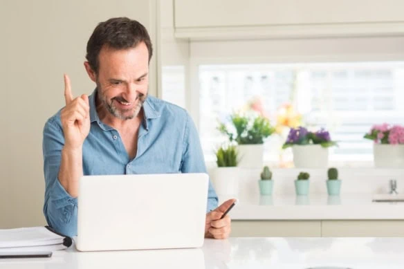 Middle age man using laptop at home surprised with an idea or question pointing finger with happy face, number one