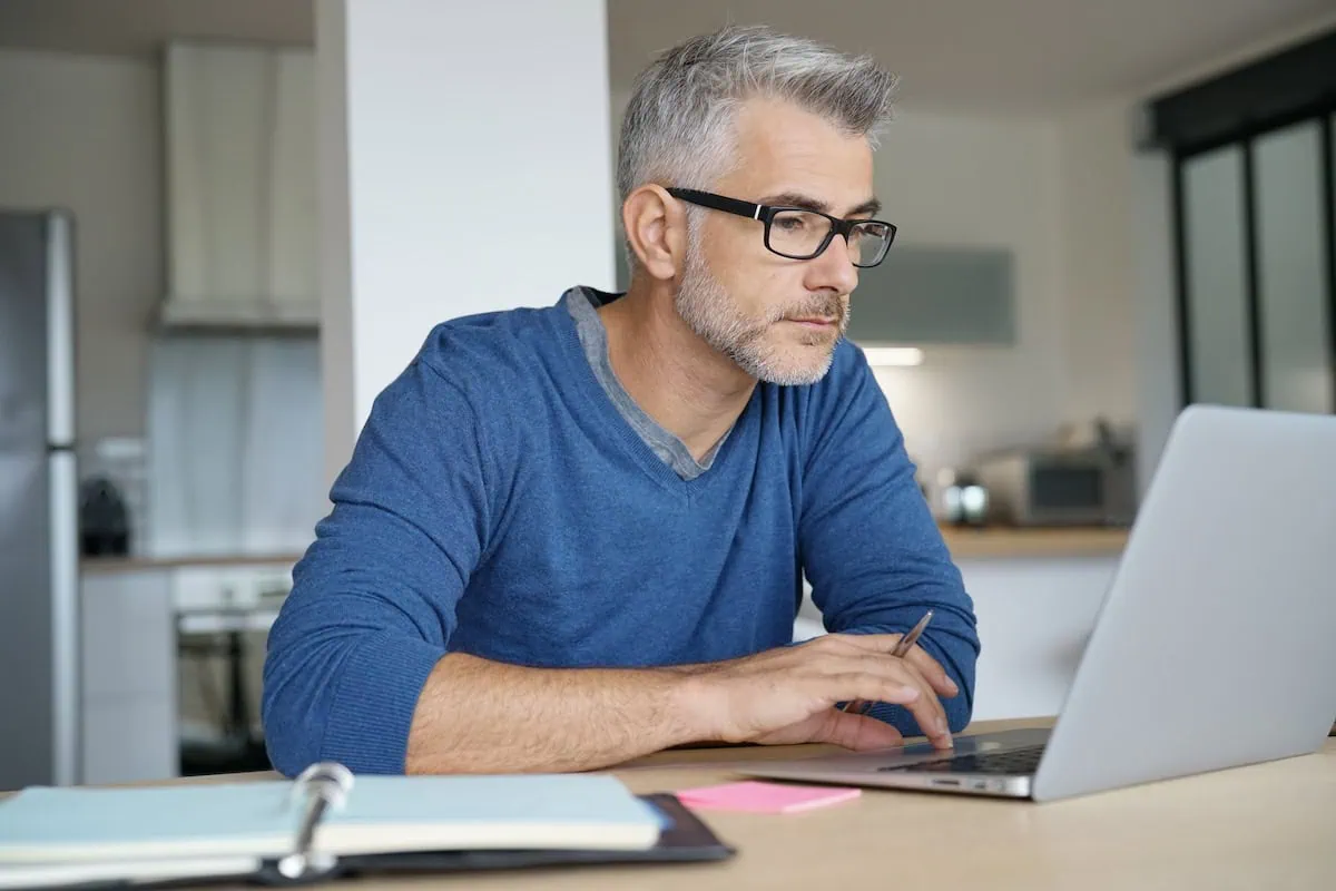 Goodbye, Commute: 12 High-Paying Jobs That Let You Work From Home 7 middle aged man looking at laptop with notebook taking notes