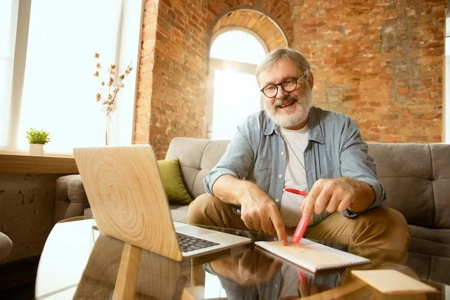 middle-aged man senior looking at laptp and notepad smiling