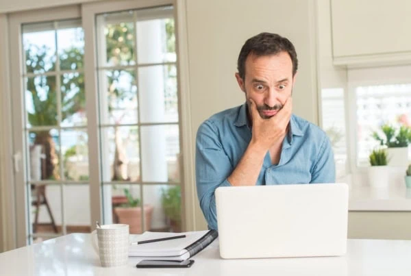 middle aged man shocked while looking at laptop at kitchen counter