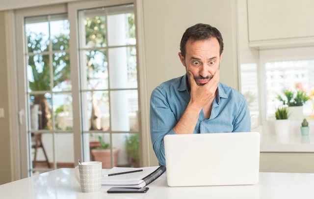 middle aged man shocked while looking at laptop at kitchen counter