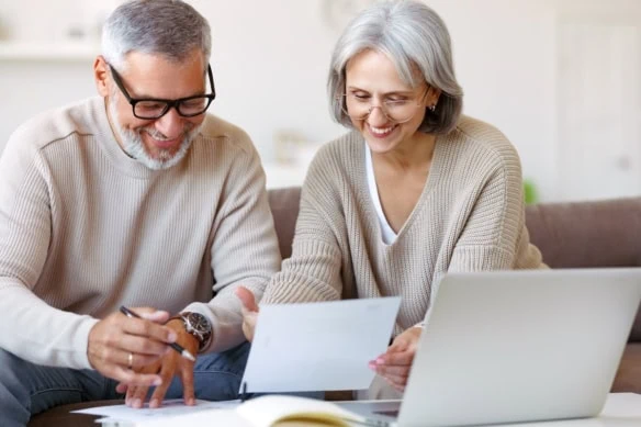 Smiling senior couple reading notification letter with good news from bank while sitting with laptop-1200