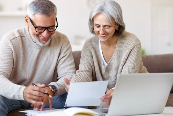 Smiling senior couple reading notification letter with good news from bank while sitting with laptop-1200