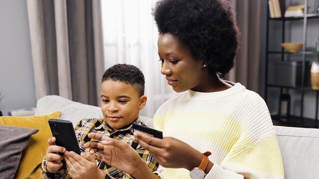 Acorns Early vs. Greenlight: Who Has the Best Prepaid Debit Card? 19 mother and son using a debit card on a phone