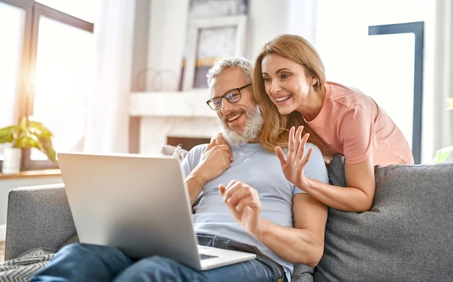 Mature couple is sitting on the couch at home with a laptop. Stay home concept. Conversation on a video call