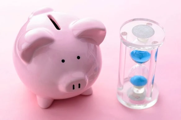 a piggy bank sits next to a small hourglass.