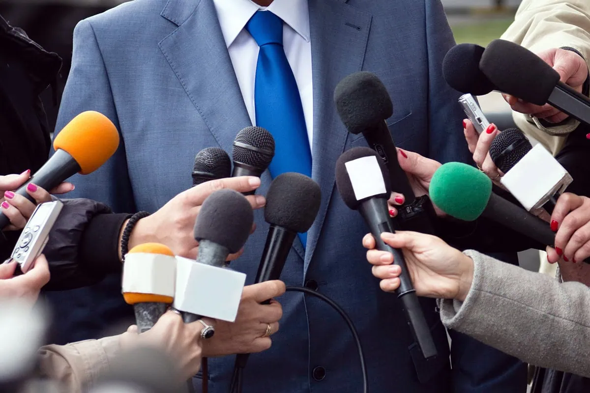 a man in a suit talks into a number of microphones.