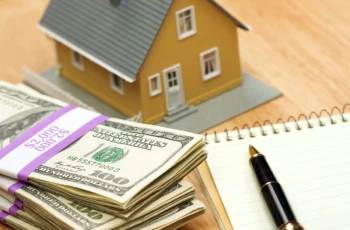 a model house sits on a table near stacks of cash.