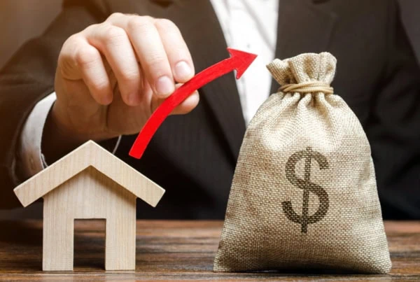 a man draws a virtual arrow from a model of a house to a small sack of cash.