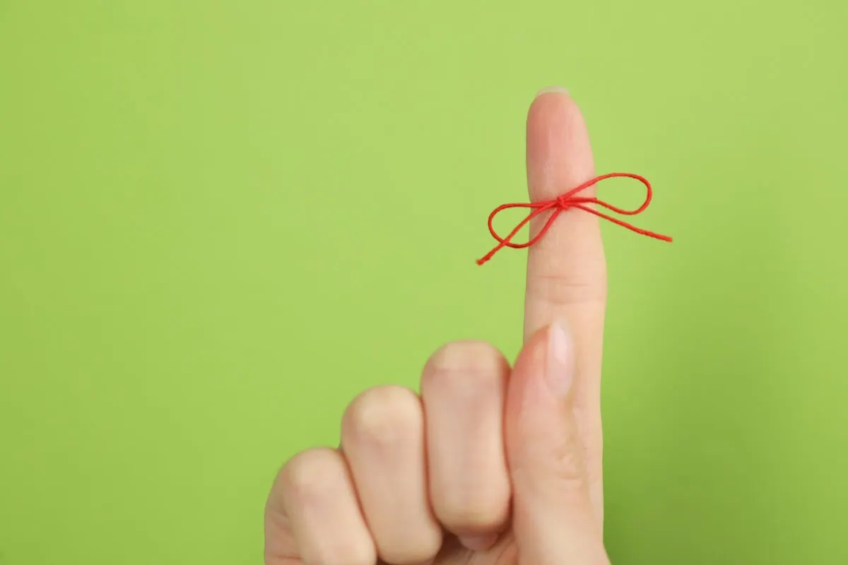Woman showing index finger with tied red bow as reminder