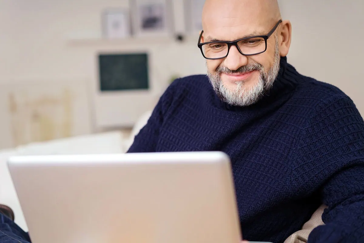 a man wearing a blue sweater looking at his laptop.