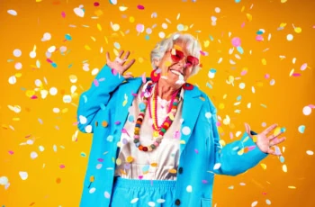 a senior woman wearing an oversized blue suit celebrates around confetti.