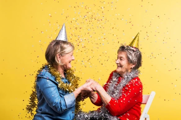 two women celebrate while wearing party hats and being sprinkled with confetti.