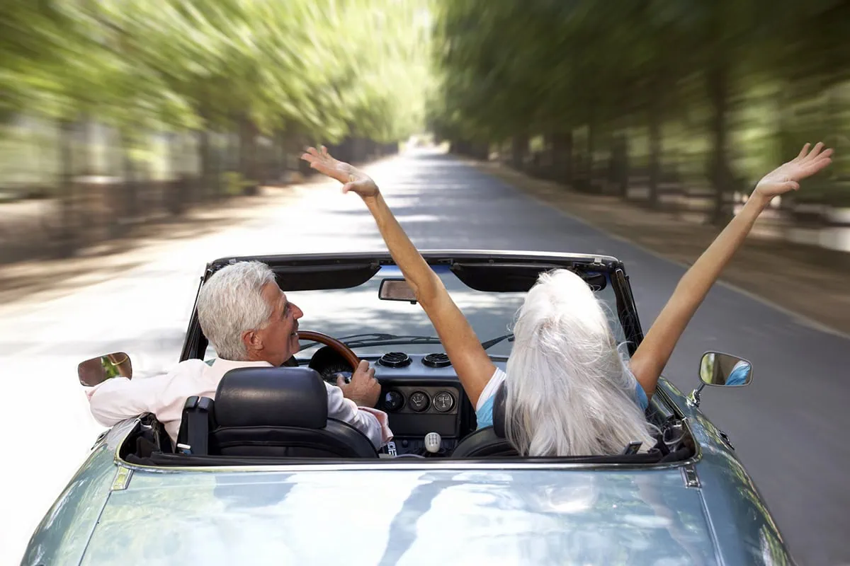 a senior man and woman drive around in a convertible.