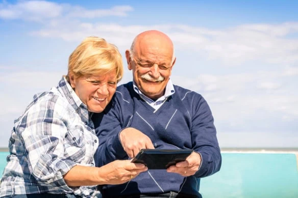 a couple looks at a tablet while sitting by the beach on a sunny day.