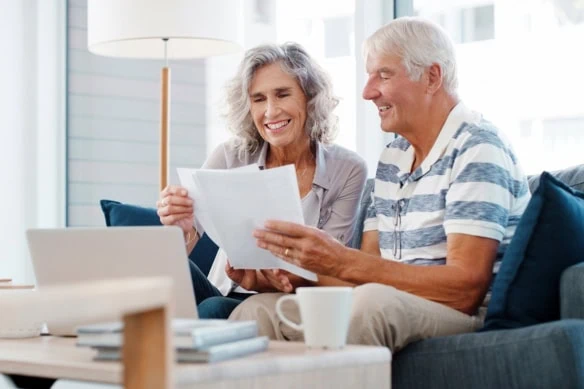 a senior couple smiles while looking at financial documents.