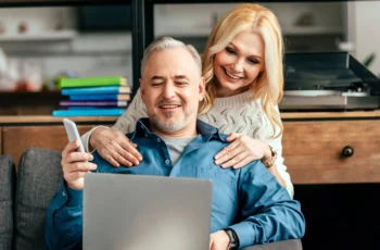 an older couple smiles while looking at their computer.