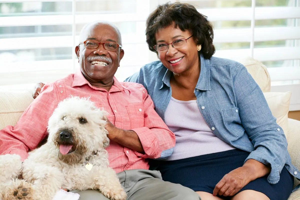 Trading Coworkers for Canines: Is a Pet the Perfect Golden Years Companion? 2 a happy senior couple sitting on the sofa with their dog. 1200