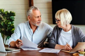 a middle-aged couple fills out documents at their table.