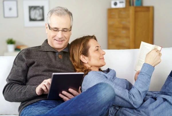 a middle-aged man and his wife lie on a couch reading.