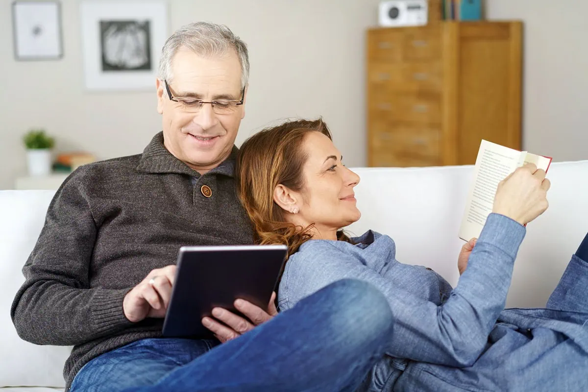 a middle-aged man and his wife lie on a couch reading.