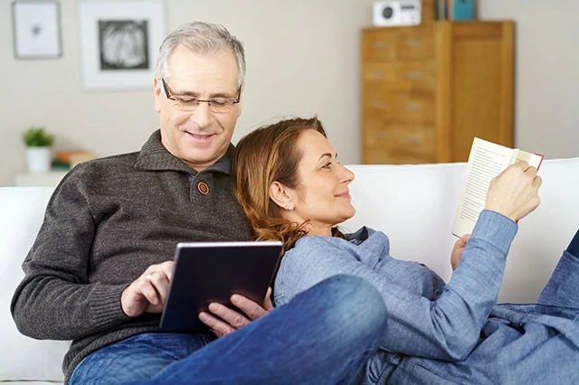 a middle-aged man and his wife lie on a couch reading.