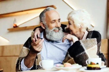 an older couple cuddles on the couch under a shawl.