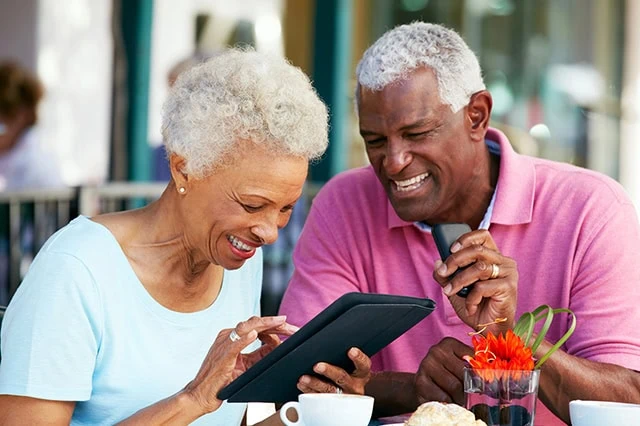 an older couple smiles while looking at a tablet computer.