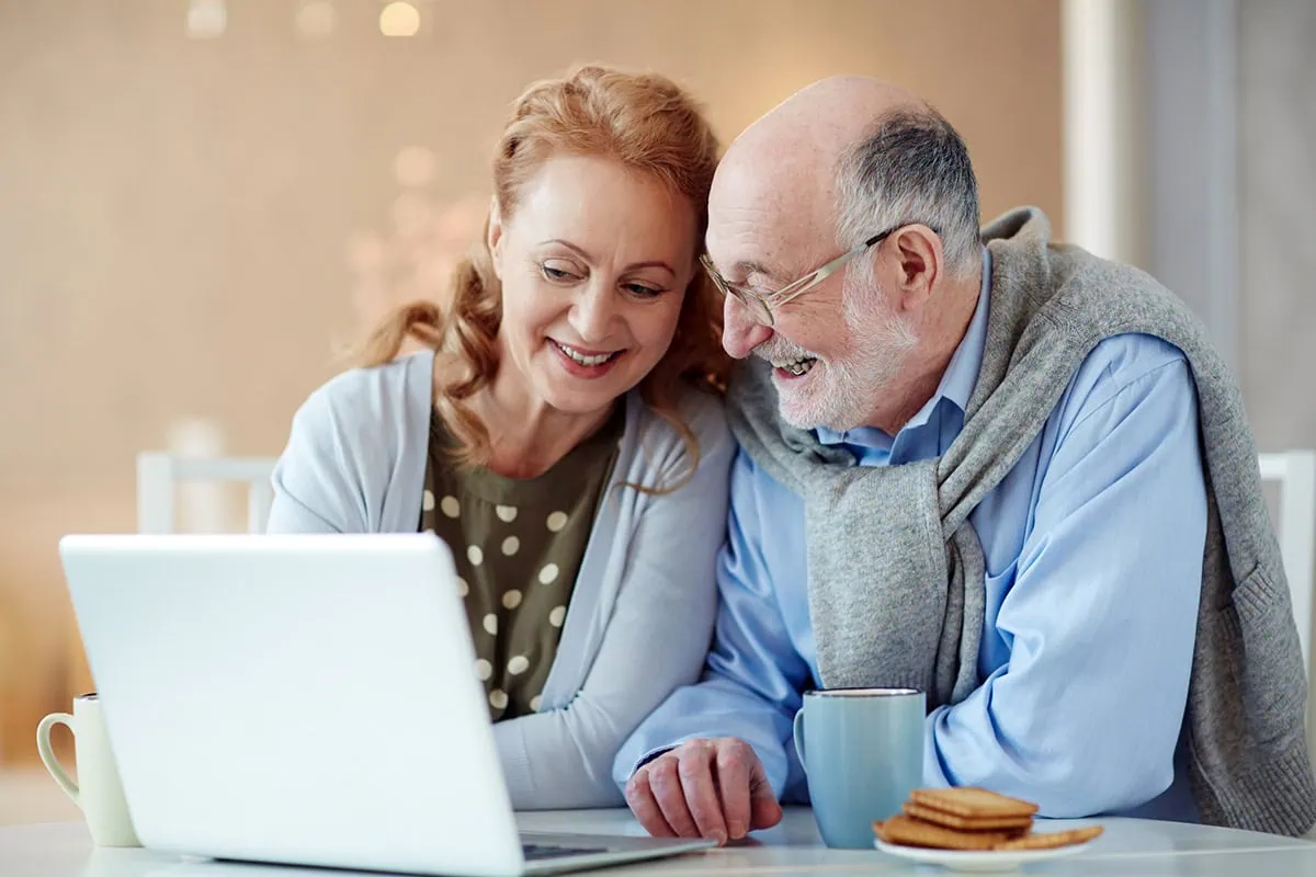 Don't Believe These 10 Popular Aging Myths 2 couple looks at a laptop while drinking tea and eating biscuits.