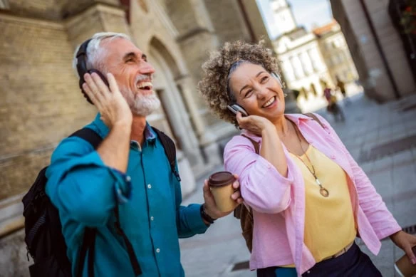 a happy senior couple listens to headphones on a walking tour of a european city.