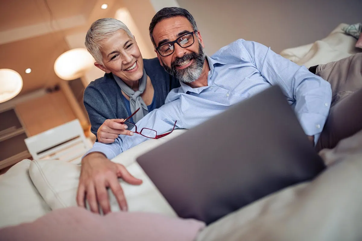 an older couple smiles while looking at their laptop.
