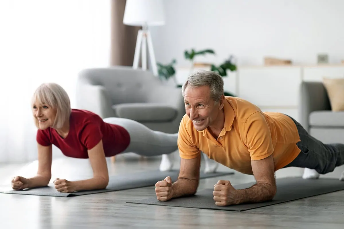 The Aging Audit: 10 Outdated Beliefs About Aging That Are Holding You Back 9 Cheerful athletic mature couple working out in their living room.